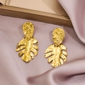 Close-up of golden monstera leaf earrings with hammered texture on purple silk fabric - 1296-Gold Monstera Leaf