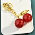 Sparkly red cherry keychain with gold metal clasp and green leaf on white display tray - Red