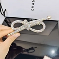 Close-up of golden rhinestone bow hair clip held against a luxury gift bag - AB Rhinestone Style
