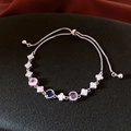 Detail of adjustable silver bracelet with colorful zircons and flower charms on black surface - Silver
