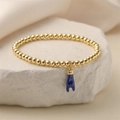 Gedetailleerde opname van gouden kralenarmband met blauwe Figa-hanger op een steen - Blauw