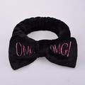 Black plush headband with a large bow featuring pink OMG embroidery on a white background - Black