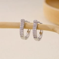 Close-up of silver U-shaped earrings set with rows of sparkling zircon on wooden branch - U-shaped Multi-row Pavé Zirconia Huggie-Silver