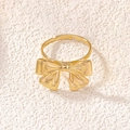 Close-up of golden bow-knot ring with adjustable open band on elegant soft fabric - Bow