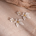Detailed close-up of matte white floral earrings with golden pistils on a warm rock base - Flower Drop Earrings (Steel Pin) / White