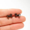 Close-up of matte black running horse stud earrings with heart cutout held in hand - Black