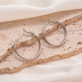 Close-up of double hoop earrings in polished silver finish on a marble texture - Double Layer Faceted Style / Silver