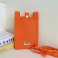 Close-up of bright orange knitted phone bag with metal button closure and fabric label - Orange