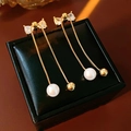 Detalle de pendientes de lazo dorado con perlas y pedrería en caja de cuero negro - Dorado