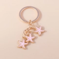 Detailopname van gouden zeesterhangers met roze emaille afwerking aan een sleutelring - Roze
