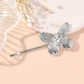 Barrette papillon en métal argenté avec détails texturés sur fond rose doux - Argenté