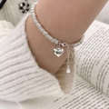 Schickes mehrlagiges silbernes Herz-Anhänger-Armband am Handgelenk mit Strickpullover-Hintergrund - Herz Anhänger Armband (SL0470)