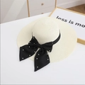 Detailed top view of wide brim straw hat with black bow and pearl accents on white surface - M / Cream