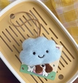 Macro shot of cute light blue plush cloud charm with embroidered smile and hanging strap - Blue