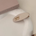 Elegant beige oval hair clip with a small gold bow detail on an aesthetic white tray - Off-white