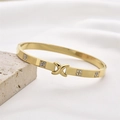 Goldener Edelstahlarmreif mit X-Verschluss und Diamantakzenten auf Steinuntergrund - Poliertes X & Strass