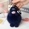 Macro shot of fluffy navy blue fox fur pompom pendant with a knitted baby doll charm - Blue