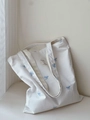 Detail van blauw strikborduursel en binnenlabel op een gestreepte katoenen canvas draagtas - Witte Basis met Blauwe Strik