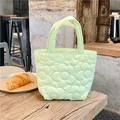 Detalle del bolso acolchado verde menta con flores sobre una mesa de madera rústica - Verde
