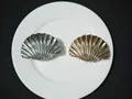 Top view of two shell-shaped metal hair claws in gold and silver finish on a plate - Small / Silver