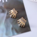 Close-up of golden crown stud earrings with sparkling crystals on a magazine - D6 Gold Crown