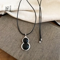 Detail of leather gourd pendant necklace with silver metal trim on textured book - Black