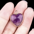 Natural purple amethyst heart pendant with gold plated rim shown on fingertip - Amethyst Gold Edging