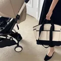 Black and beige canvas diaper bag with multiple pockets shown next to a stroller - Black
