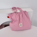 Detailed macro view of the pink pleated fabric texture and stitched brand label on the tote bag - Pink