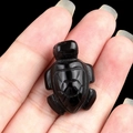 Miniature hand-carved black obsidian turtle figurine shown on a hand for scale - Obsidian
