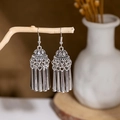 Detail shot of silver ethnic tassel earrings hanging on a natural wooden stand - E2874-19/Cylindrical Tassel