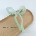 Minimalist matte mint green bow-shaped hair claw clip with jelly texture on wood tray - Matte Jelly Light Green