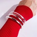 Set aus vier polierten silbernen Armreifen, getragen über einem roten Strickpullover-Ärmel - Silber