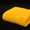 Absorbent yellow cotton bath towel with textured border, neatly folded on black background - Gold Yellow
