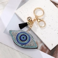 Macro shot of evil eye heart charm with blue rhinestones and black fringe tassel - Black Eye Gold Clasp