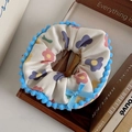 Details von Plüsch-Haargummi mit Blumenmuster, blauer Schleife und Bommeln auf Holztablett - Blumig Blau Rand Scrunchie