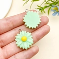 Green resin daisy charm with yellow core for DIY jewelry making shown on hand - Light Green