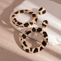 Detalle de pendientes de aro de leopardo en soporte de piedra con sombras estéticas - Pendientes colgantes de cuero con estampado de leopardo