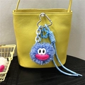 Detailed view of a blue plush monster charm with heart hook and cord on a yellow leather bag - Sky Blue