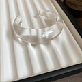 Close-up of a chunky transparent resin wave bangle on a white textured display tray - Clear
