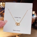 Détail de pendentifs cœurs dorés entrelacés sur une chaîne fine et sa carte - X025 Or 18K Doubles Cœurs Entrelacés