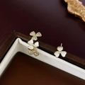 Detalle de pendientes asimétricos de flores con circonitas y perlas en un joyero marrón - Flor Asimétrica Dorada (Pin de Plata)