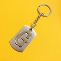 Detail shot of a silver stainless steel keychain with hollow G-letter design on yellow background - Letter G