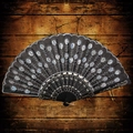 Elegant black hand fan with white embroidery and silver sequins on dark wood background - White
