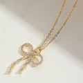 Collier nœud doré élégant orné de zircons brillants sur une surface crème texturée - Nœud Papillon Long
