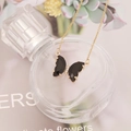 Close-up of gold butterfly pendant with black wings and crystal accents on perfume bottle - Black