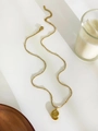 Detail van een gouden spiraalvormige schelphanger aan een fijne kralenketting - Gouden Wulk