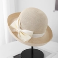 Close-up of elegant straw sun hat with a large cream silk bow on a minimalist display - Beige