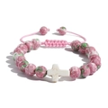 Dettaglio delle perle floreali rosa e del ciondolo a croce sul bracciale intrecciato - Pietra di Pioggia + Croce Bianca