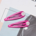 Detail view of two pink drop-shaped metal hair clips with cloud pattern accents on a magazine - Rose Red